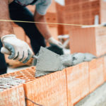 Professional worker using pan knife for building brick walls with cement and mortar
